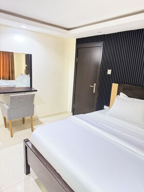 A hotel room with a bed, a desk, a chair, a wardrobe, and a mirror. - Floyd Msquare Hotel (Lagos)