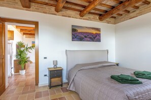 A bedroom with a bed, a nightstand, a lamp, a potted plant, and a painting on the wall. - Antica Dimora delle Tre Coste (Marche)