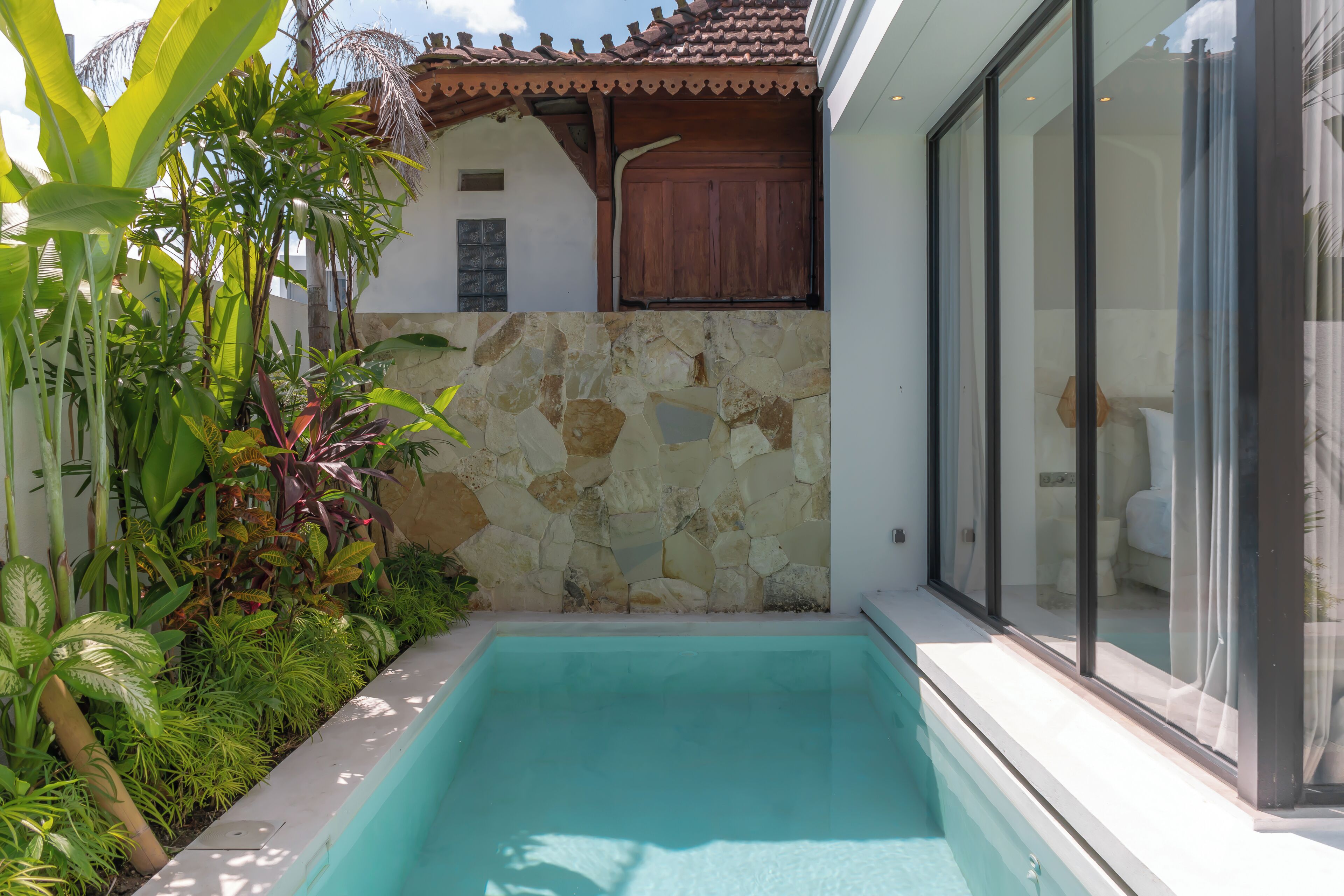 A swimming pool with a stone wall and tropical plants.
