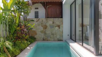 A swimming pool with a stone wall and tropical plants.