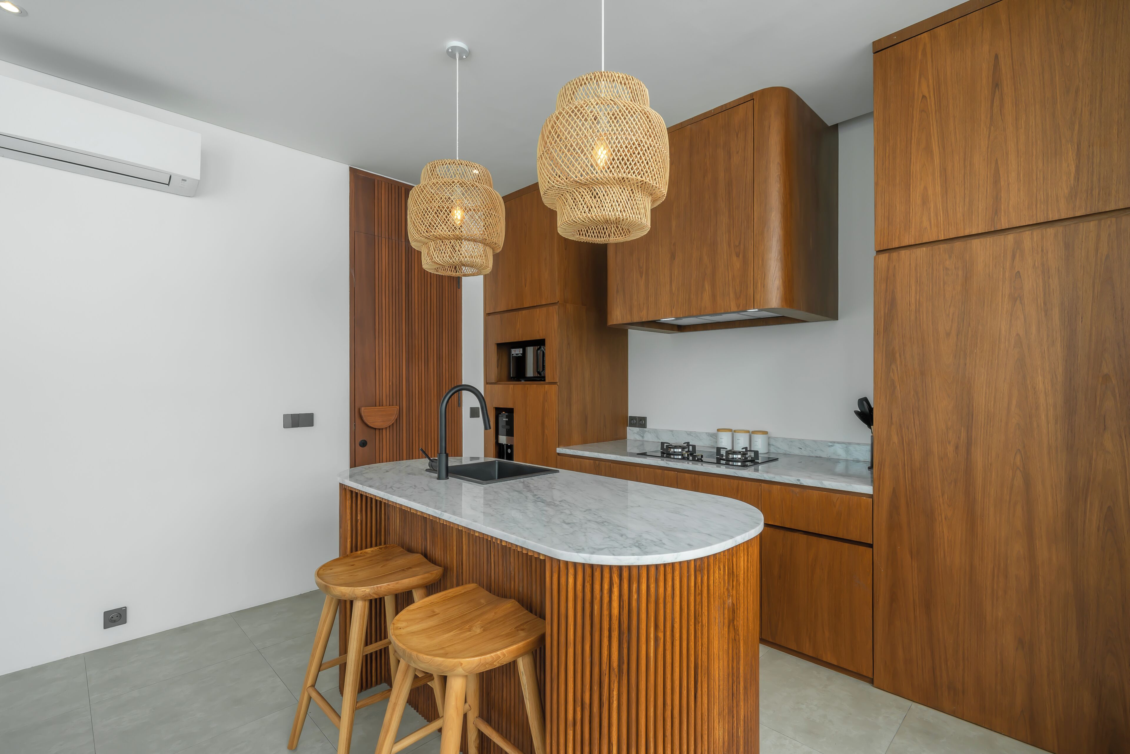 Une cuisine moderne dotée d’un îlot central, de meubles en bois et de deux suspensions en osier.