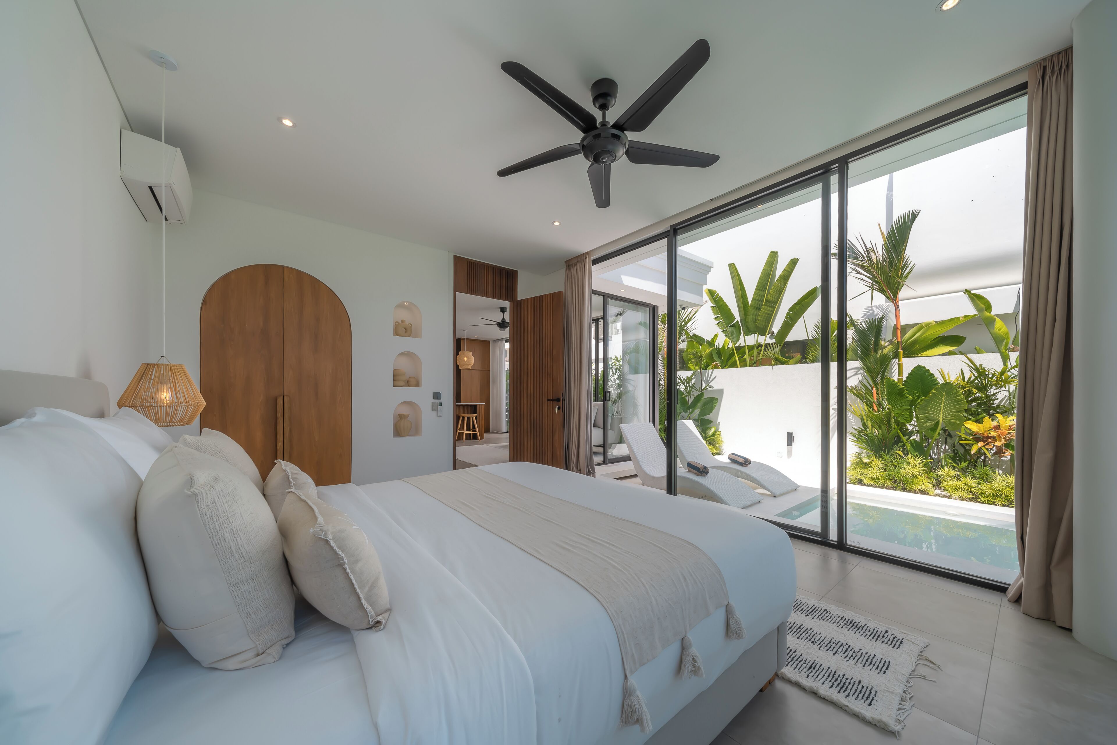 Une chambre moderne avec un grand lit, un ventilateur de plafond et une vue sur une piscine et un jardin.