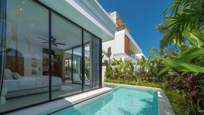 Una casa moderna con un soggiorno vetrato, una piscina e piante tropicali.