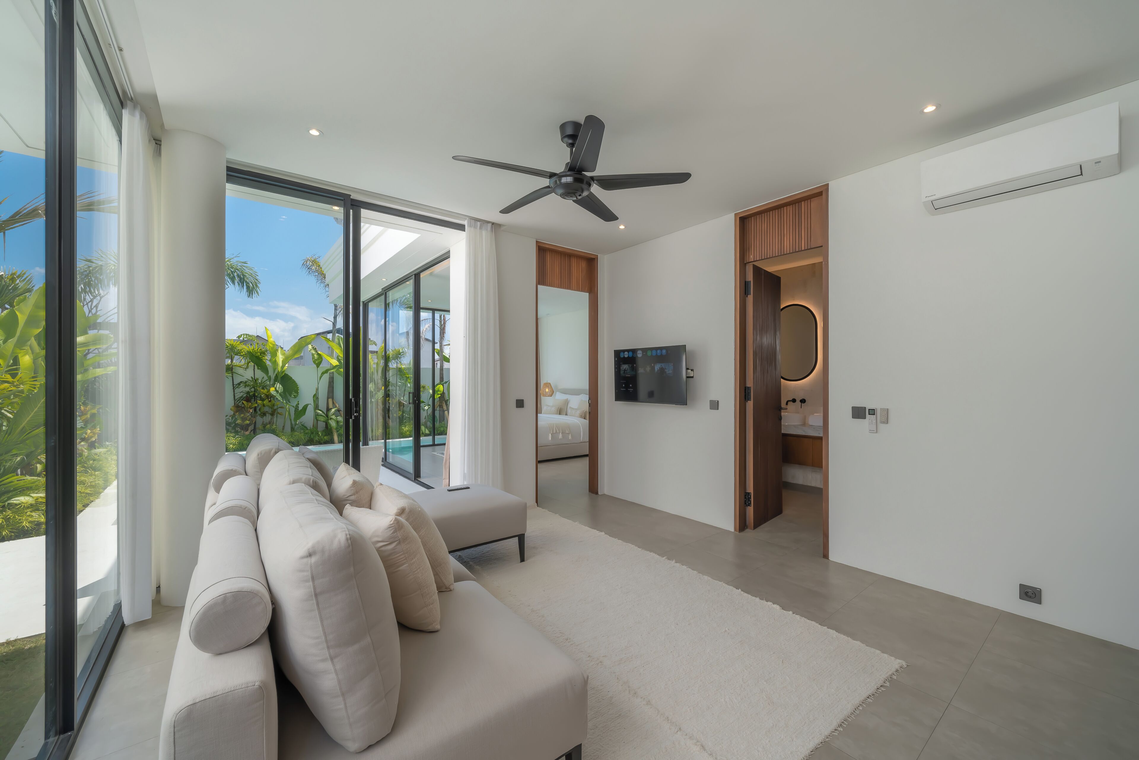 A modern living room with a large sofa, a ceiling fan, and a view of a swimming pool.