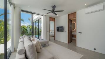 A modern living room with a large sofa, a ceiling fan, and a view of a swimming pool.