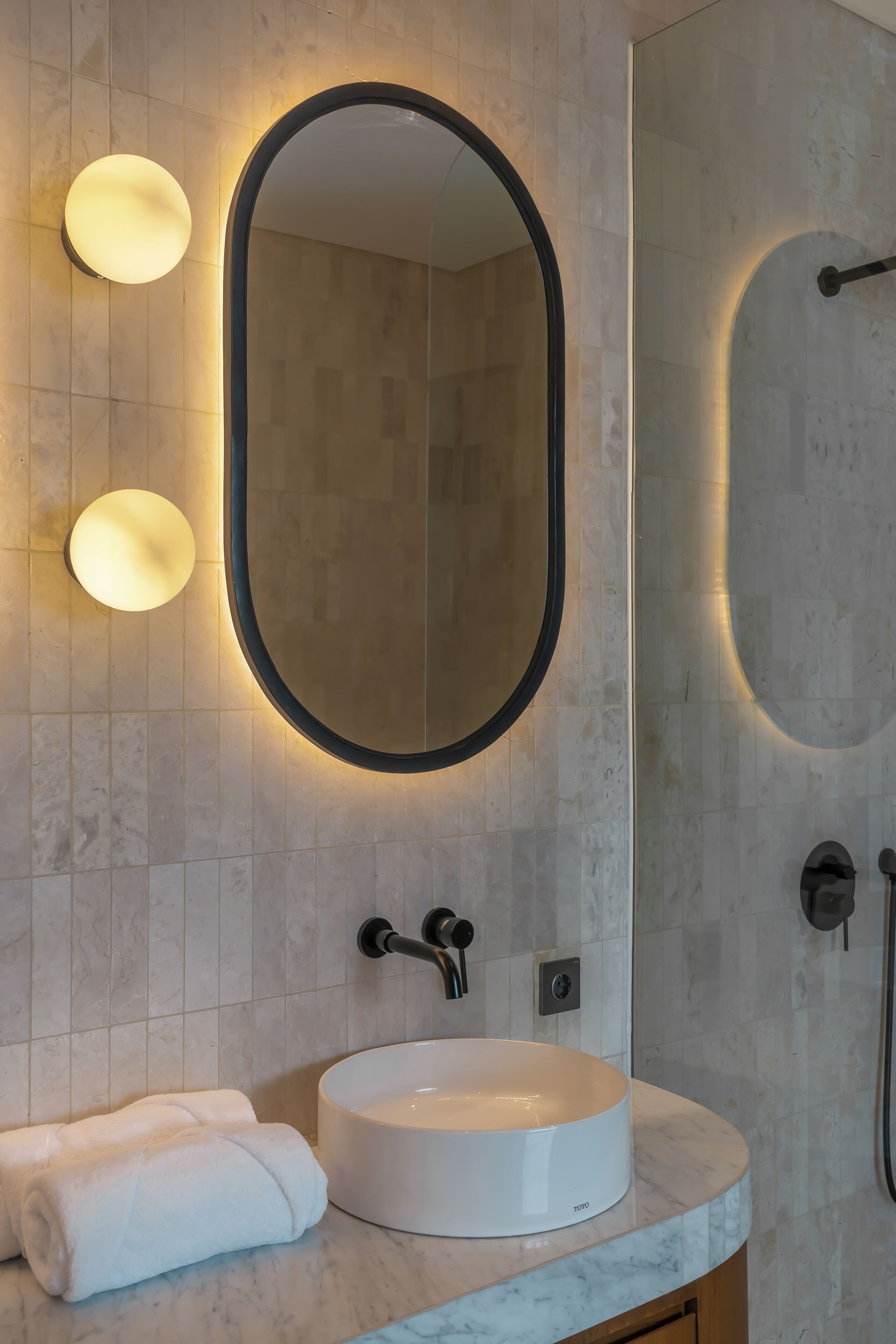 Un baño con un espejo redondo, un lavabo blanco y una toalla.