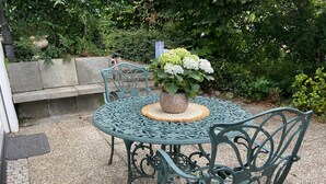 Una mesa redonda de metal con sillas, una planta en maceta y un banco en un jardín.