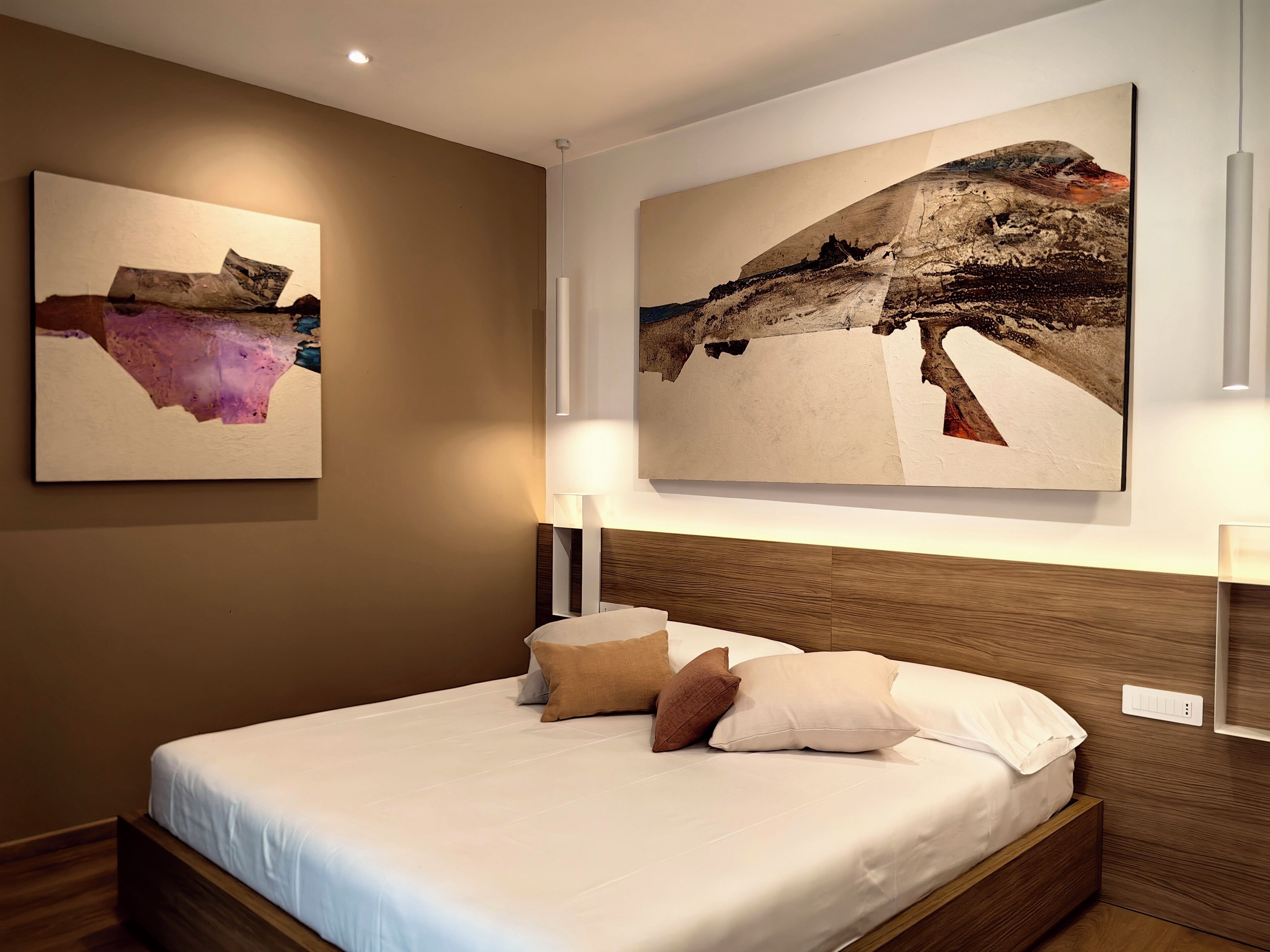 Una habitación de hotel moderna con una cama grande, dos obras de arte colgadas en la pared y un cabecero de madera.