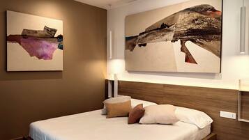 Una habitación de hotel moderna con una cama grande, dos obras de arte colgadas en la pared y un cabecero de madera.