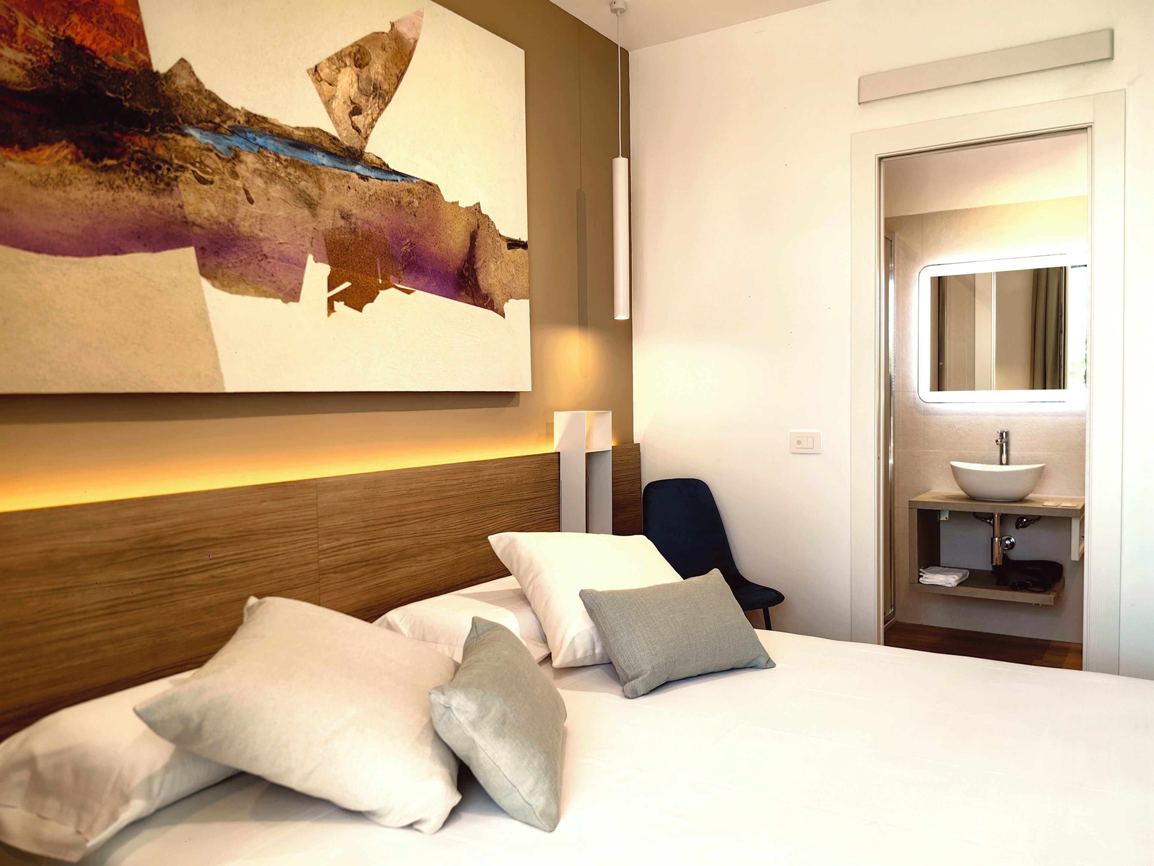 Hotelkamer met groot bed, bureau, stoel, wandkunst en badkamer met wastafel en spiegel.