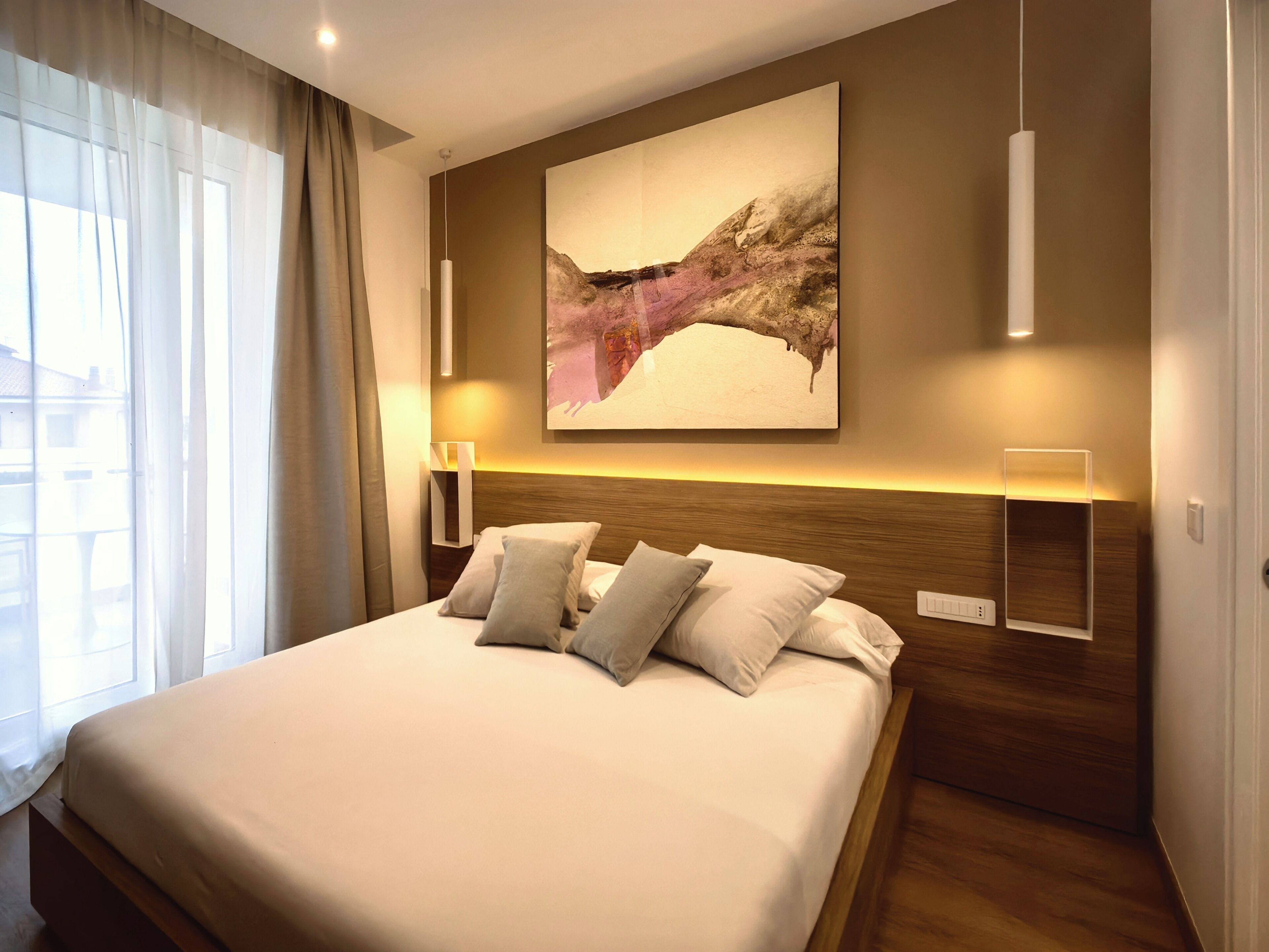 A hotel room with a large bed, a mounted artwork, bedside lamps, and a view of the outside.