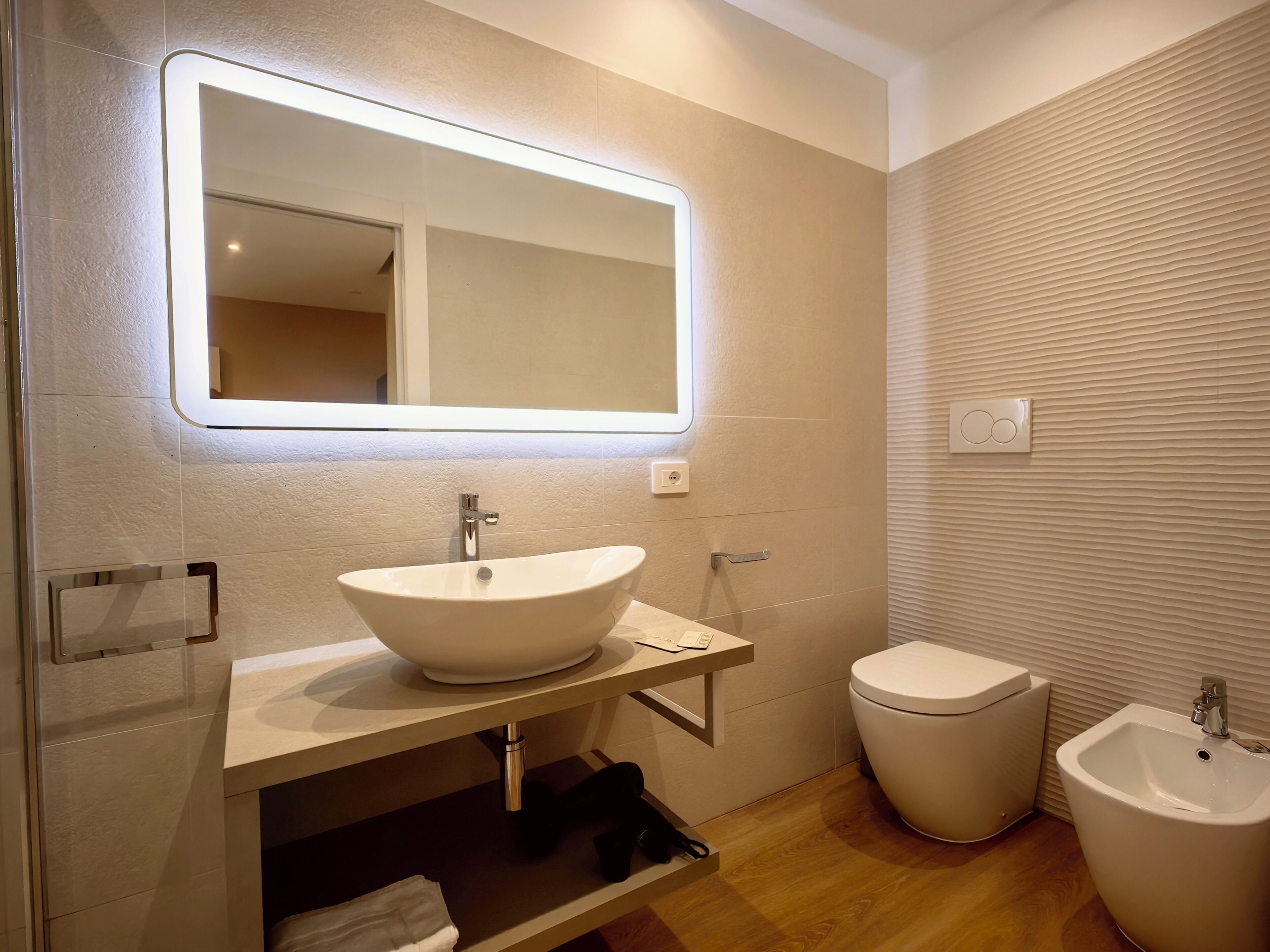 Une salle de bain moderne avec un grand miroir, un lavabo, des toilettes et un bidet.
