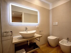 A modern bathroom with a large mirror, a sink, a toilet, and a bidet.