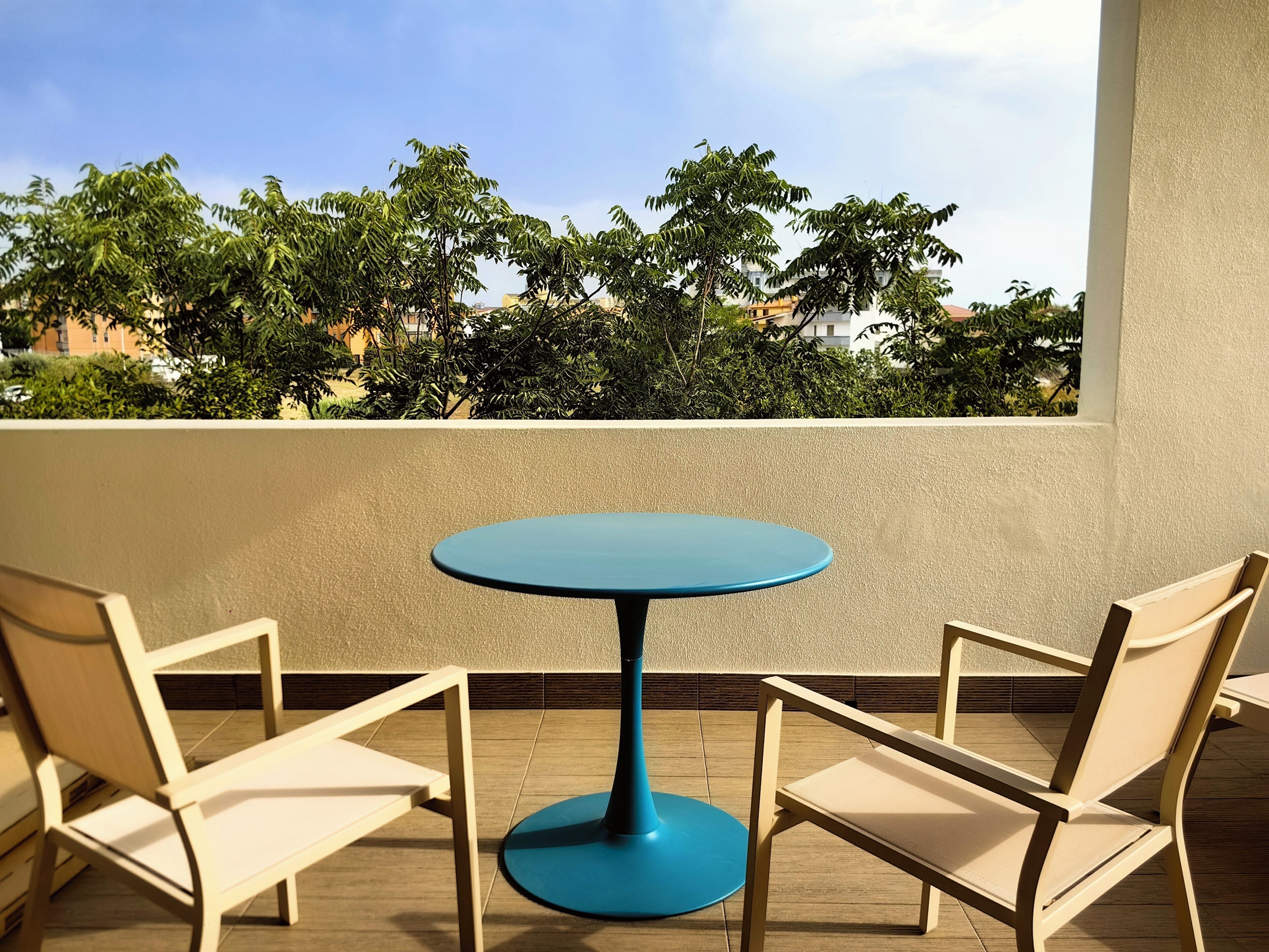 A round table with two chairs on a balcony with a view of greenery and buildings.