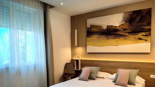 Habitación de hotel con una cama grande, cabecero, un cuadro colgado en la pared y una mesita de noche con lámpara.