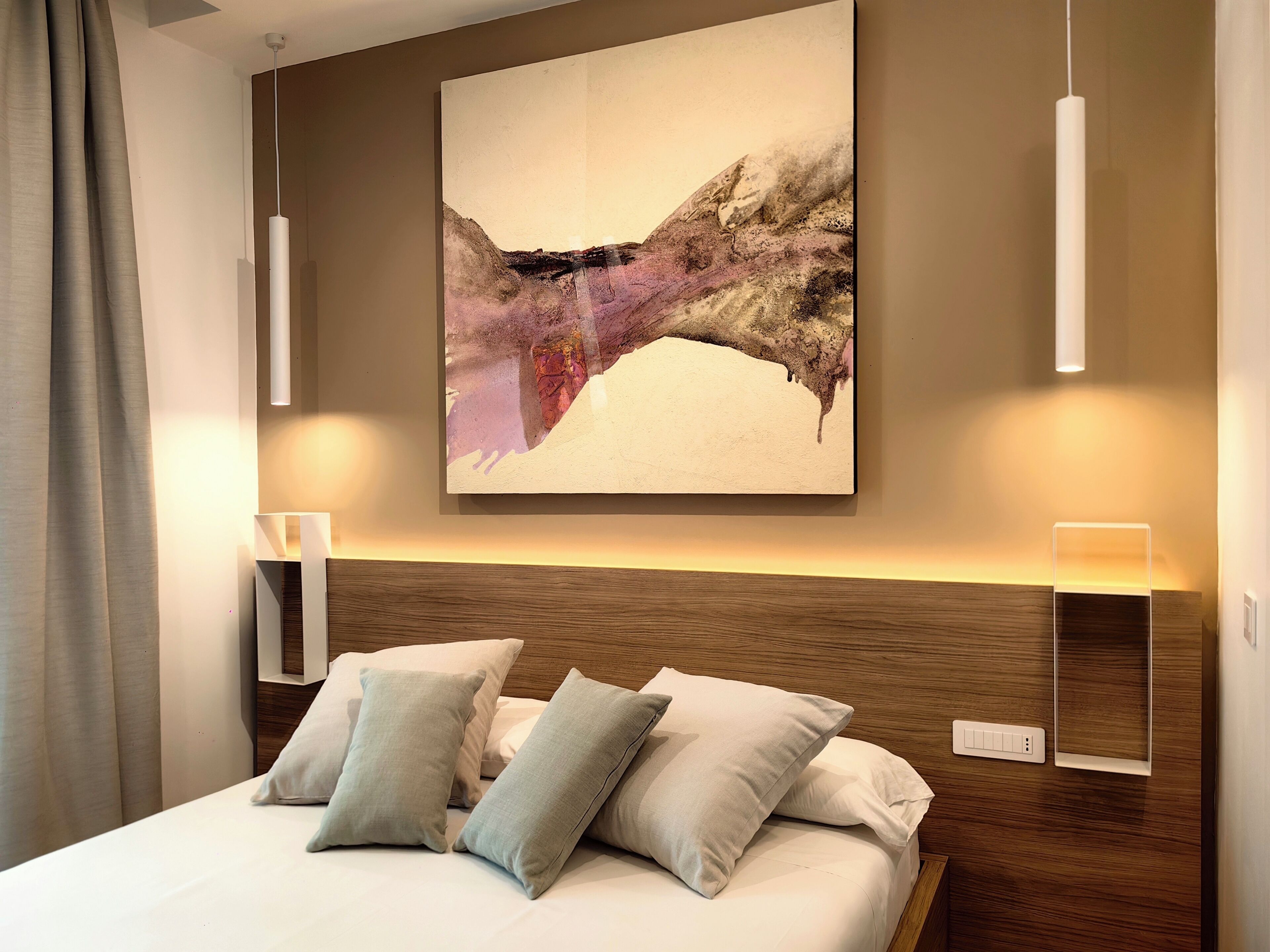 Une chambre d’hôtel moderne avec un grand tableau abstrait, une tête de lit en bois et des lampes de chevet.