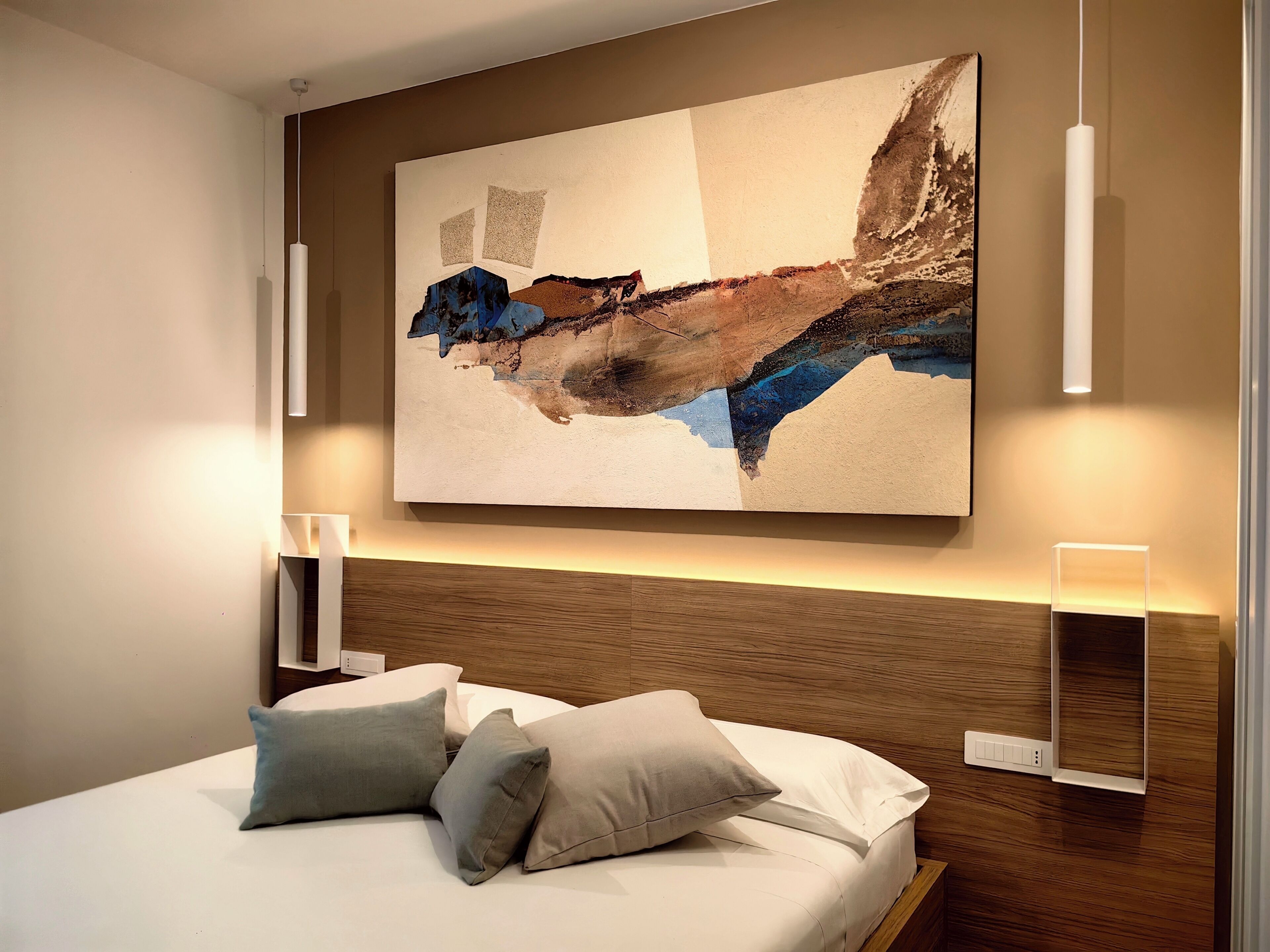 A modern hotel room with a large abstract painting, a neatly made bed with pillows, and wall-mounted lighting.