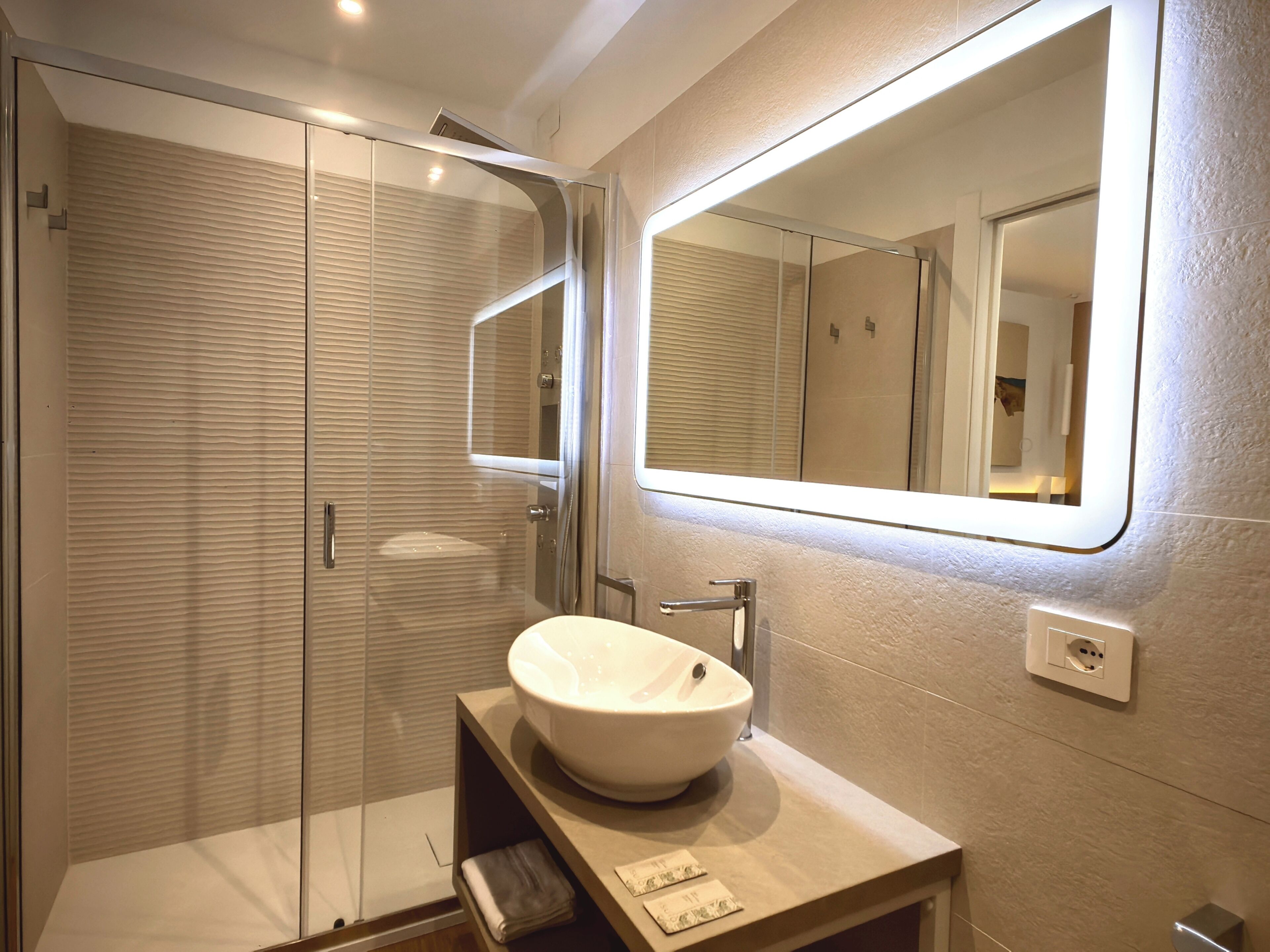 Un baño moderno con ducha de vidrio, un espejo grande y un lavamanos blanco.