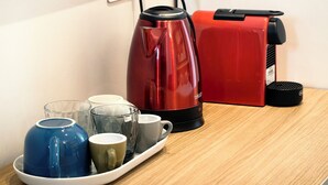 Un área de cocina con un hervidor eléctrico rojo, una cafetera roja y una bandeja con tazas variadas y una taza azul.