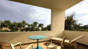 Un balcón con una mesa y dos sillas, con vistas a árboles y edificios al fondo.