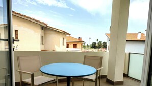 Un balcón con una mesa redonda y dos sillas, con vista a un edificio de techo a teja.