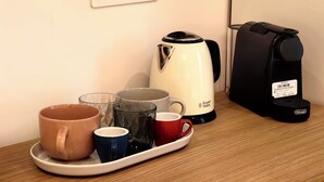 Una estación de café con hervidor, cafetera y una bandeja con tazas.