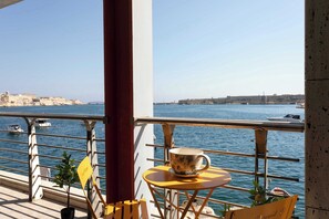 A balcony with a table and chairs overlooking a body of water, with buildings in the background.