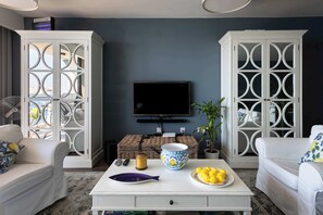 A living room with a television, white furniture, decorative items, and a view of the sea. - St Angelo Mansions 3BDR flat with Seaview (Birgu)