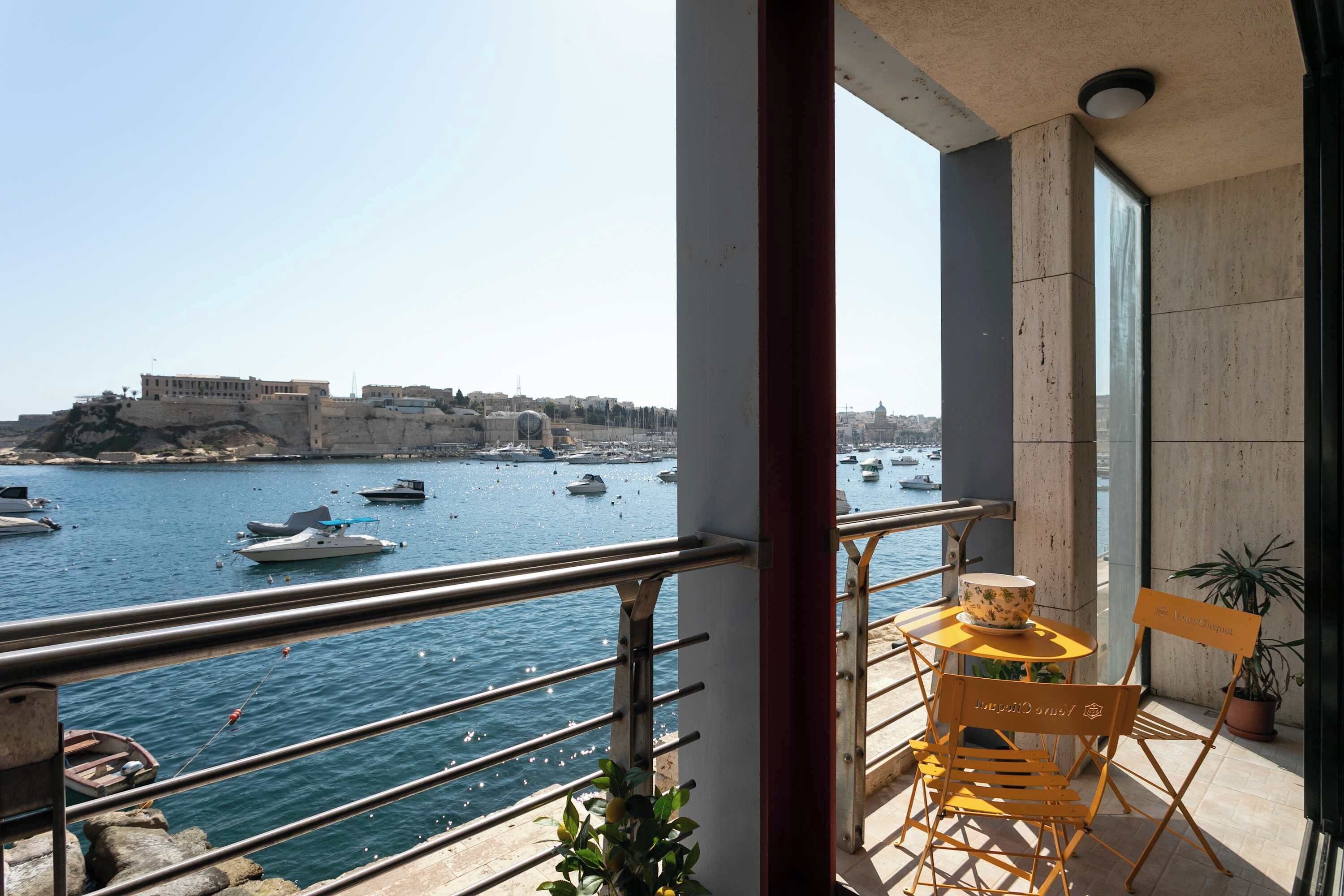 Een balkon met uitzicht op zee, een tafel met een stoel en een bloempot.