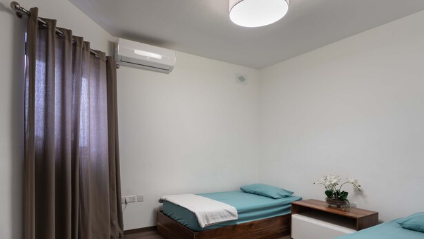 Ein Schlafzimmer mit zwei Betten, einem Deckenventilator, einer Klimaanlage und einem Nachttisch mit einer Pflanze.