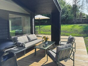 An outdoor deck with a sofa, chairs, a grill, and a table with a vase of flowers. - Newly built holiday home 200 m from beach in Mols (Ebeltoft)