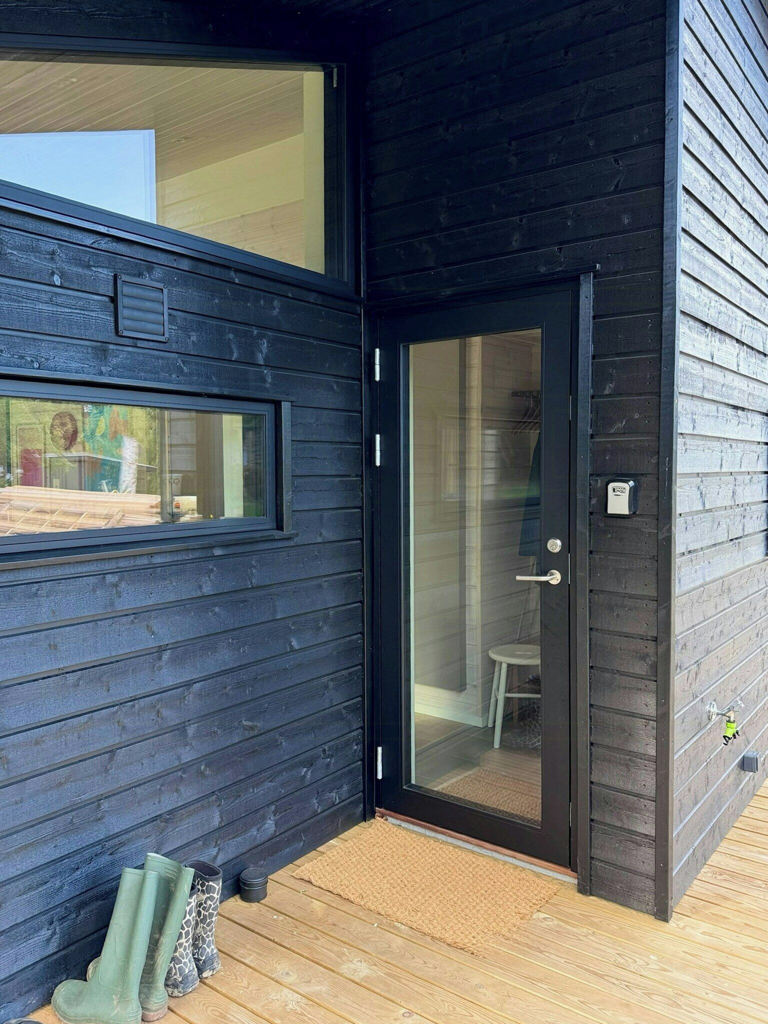 Un bâtiment moderne à l’extérieur sombre, doté d’une entrée avec une porte en verre et d’une terrasse en bois.
