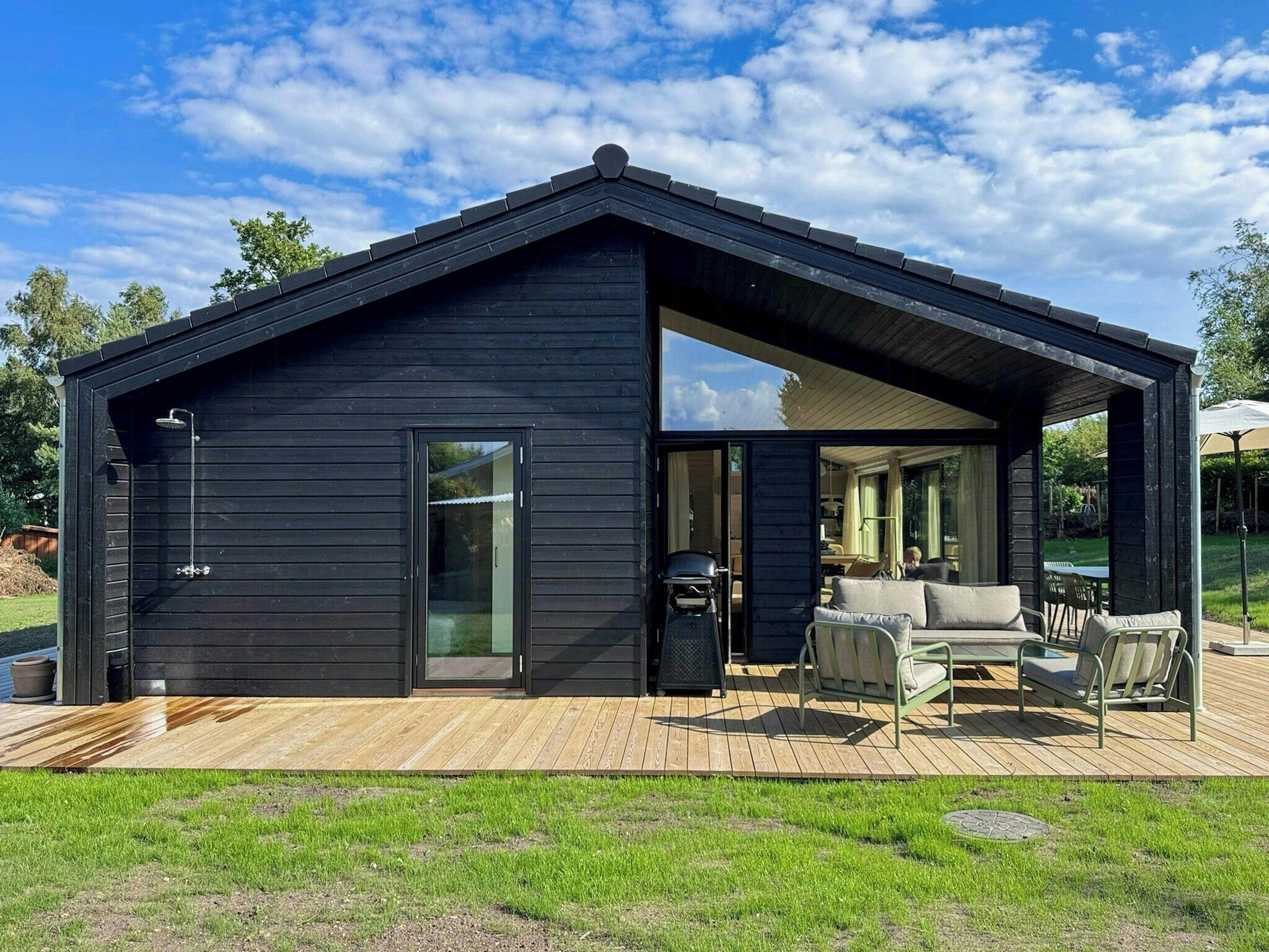Een moderne buitenstructuur met een grote schuindeur, een overdekt terras met zitplaatsen en een heldere lucht.