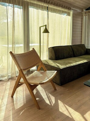 A room with a woven chair, a sofa, a floor lamp, and sheer curtains.