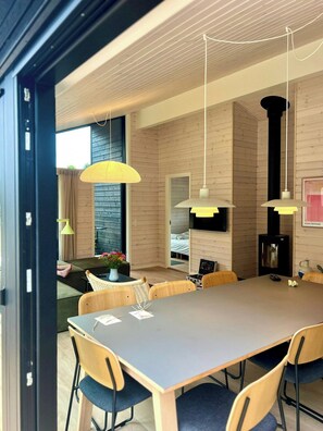 A modern dining area with a long table, multiple chairs, and pendant lighting.