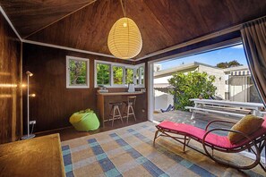 A modern interior with a wooden ceiling, a dining area with a table and chairs, a green bean bag, and a view of the outdoors. - Coastal Nostalgia – Classic charm, Coastal comfort (Macmasters Beach)