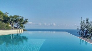 Ein Pool ohne Rand mit freiem Blick auf das Meer und ferne Berge.