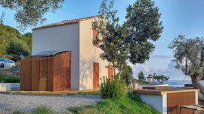 A modern building with a flat roof, a wooden fence, and a gravel driveway. - Villa with infinity pool over the Tyrrhenian Sea (Cefalù)