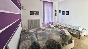 Ein Zimmer mit zwei Betten, einem Heizkörper, einem Fenster mit Vorhängen und einer Wand mit gerahmten Bildern.