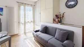 Ein modernes Wohnzimmer mit einem grauen Sofa, einem Holztisch und einem großen Fenster mit Vorhängen.