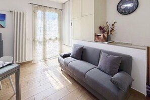 A modern living room with a grey sofa, a wooden table, and a large window with curtains. - Spacious 89 m² apartment, ideal for 6 people, located on the ground floor of a period building with a private entrance (accessible via stairs).Situated in the heart of the historic center, the property offers a splendid view of Rocca Brancaleone Park an (Ravenna)