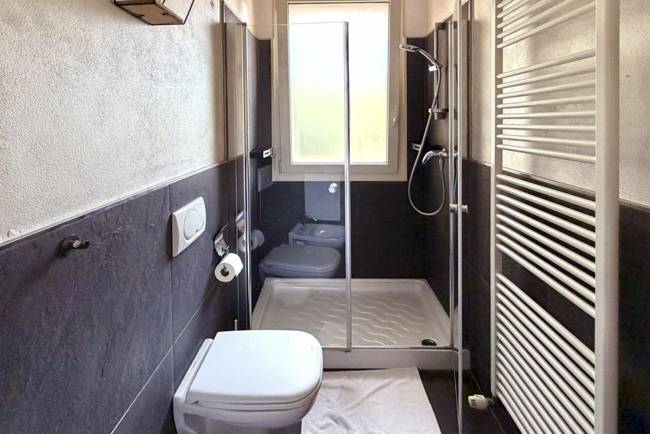 A compact bathroom with a toilet, a shower, and a small window.