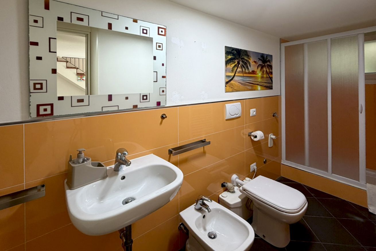 A bathroom with a sink, bidet, toilet, and a mirror with a decorative frame.