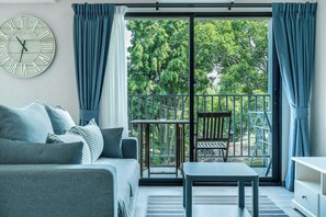 A modern living room with a sofa, a table, and a balcony with a view of trees. - The Title Residencies Naiyang Beach Apartment E413 (Thalang/Sakhu)