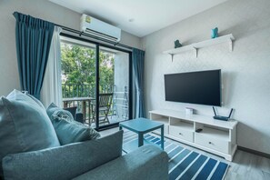 Ein modernes Wohnzimmer mit einer Couch, einem Fernseher und einem Balkon mit Vorhängen.