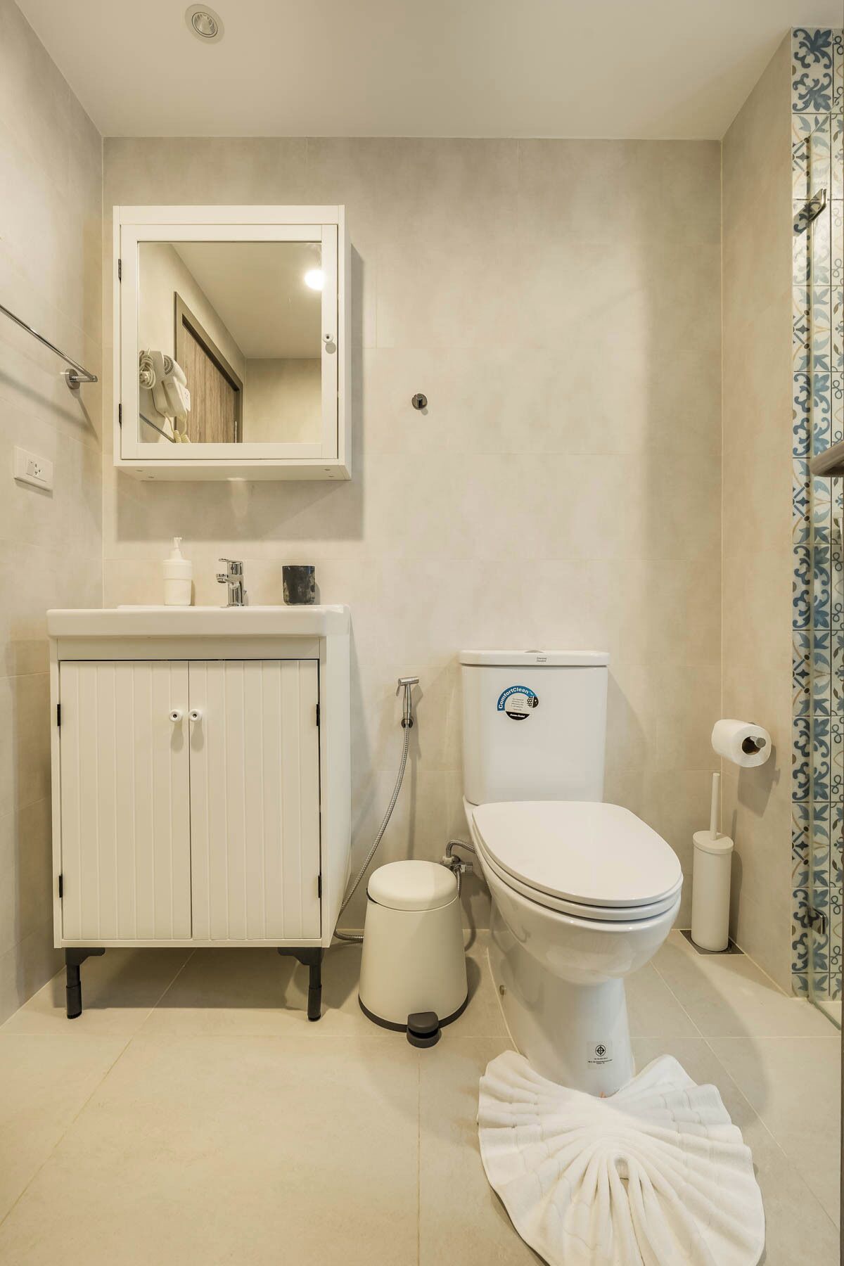 Une salle de bain comprenant des toilettes, un lavabo avec un miroir au-dessus, une poubelle et un rideau de douche.