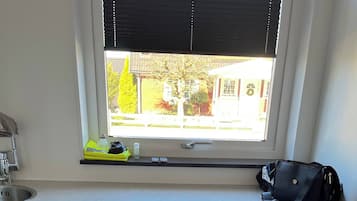 A laundry area with two white front-loading washing machines, a window with blinds, a sink, and a shelf with items.