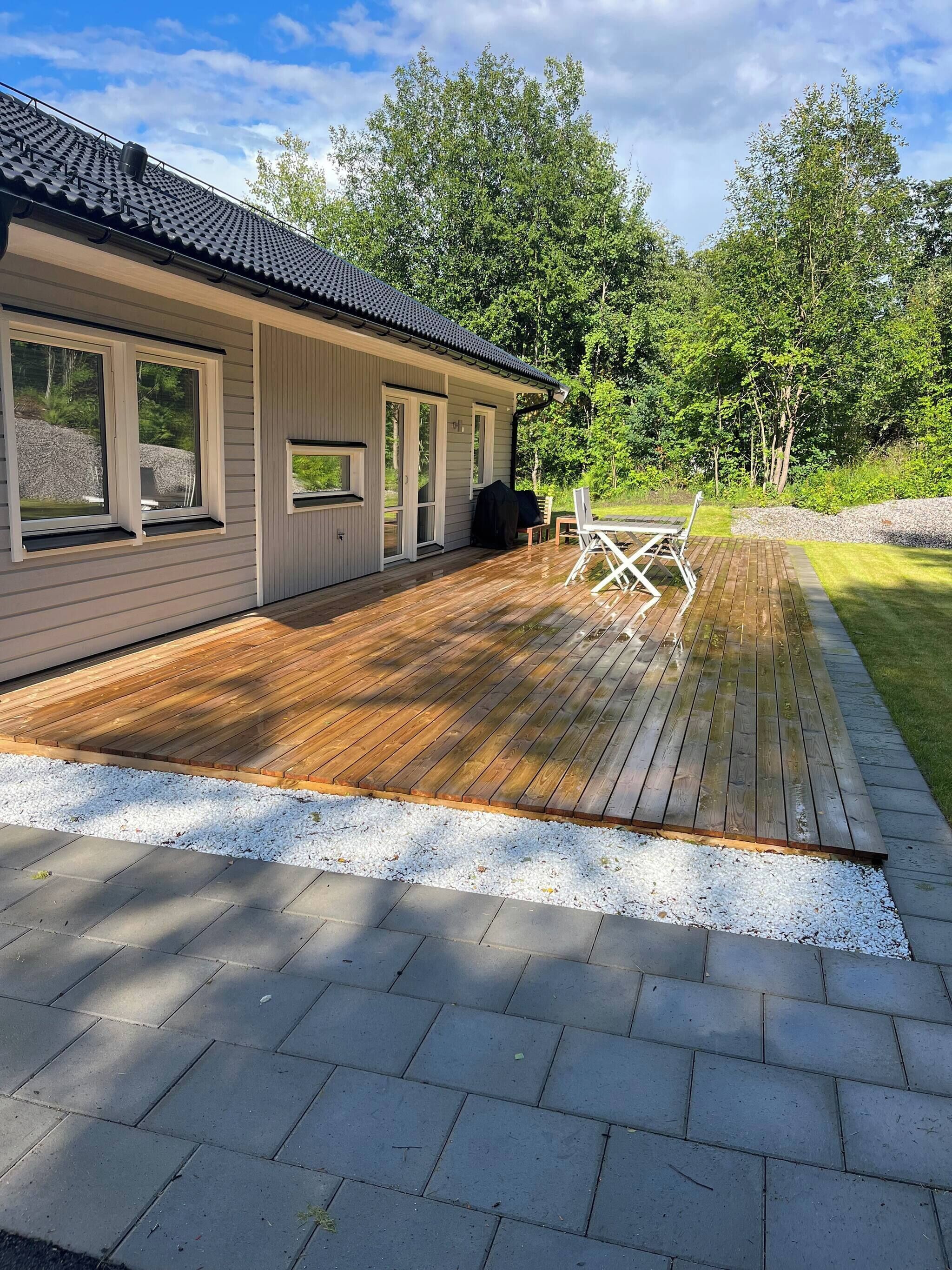 A house with a deck, a covered outdoor seating area, and a view of a grassy area with trees.