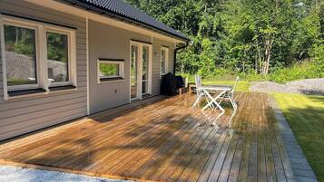 A house with a deck, a covered outdoor seating area, and a view of a grassy area with trees.