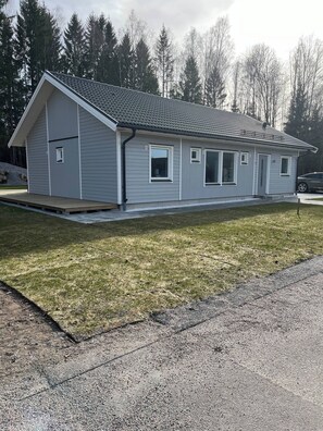 A single-story building with a gabled roof, a covered porch, and a gravel driveway. - Skeenhuset Near the Lake (Annerstad)
